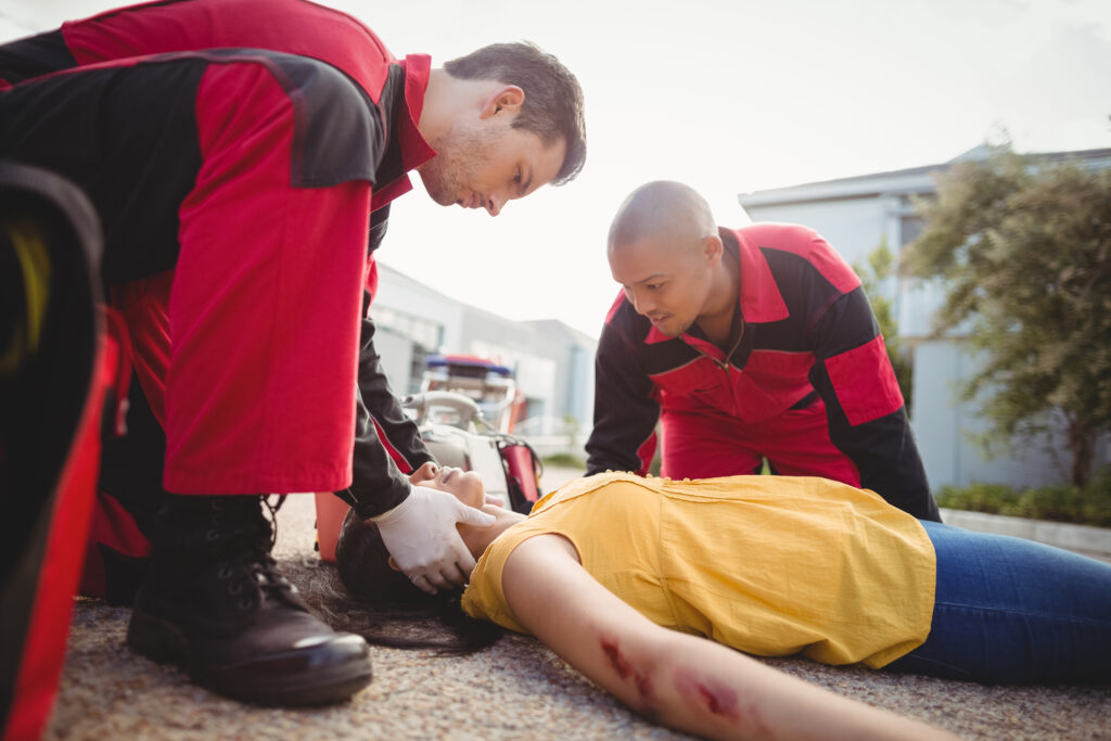 First responders in red and black uniforms stabilizing an injured woman lying on the ground, illustrating a California catastrophic injury claim handled by Protection Law Group.