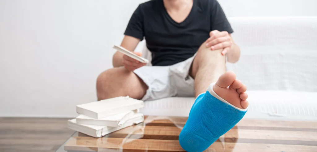Medical professional wearing gloved hands carefully supporting a patient's bandaged and casted lower leg on a medical table, representing a California broken bone injury claim handled by Protection Law Group.